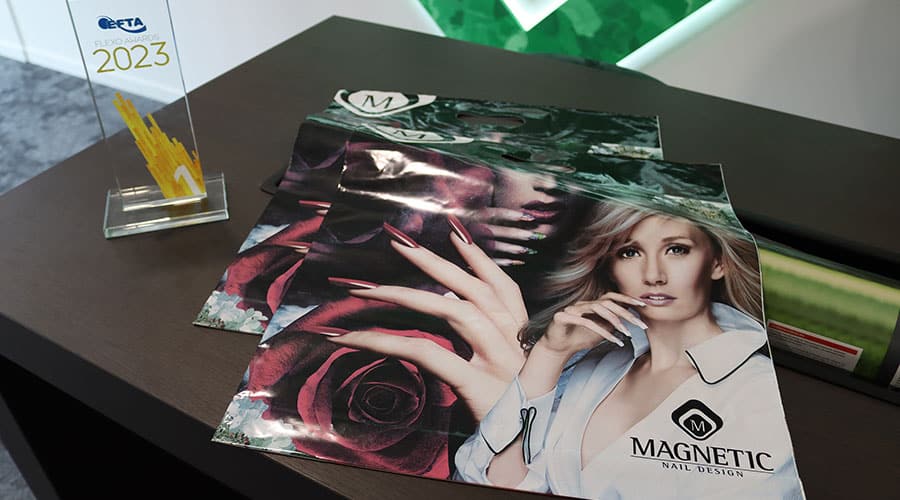 EFTA-Benelux Flexo Gold Award steht auf einem Schrank und daneben liegen zwei grpße Flyer mit einer Frau und einer Rose drauf. Aufschrift "Magnetic Nail Design"