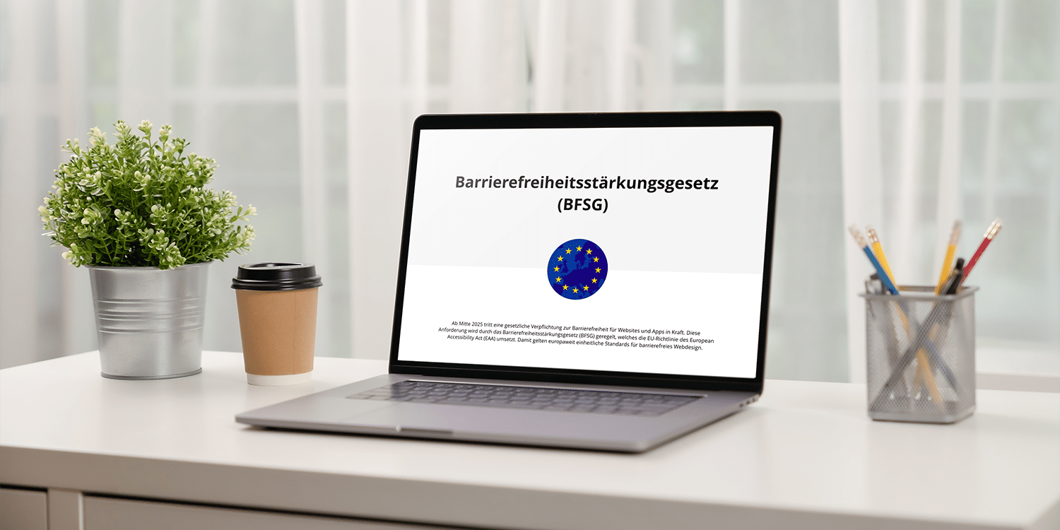 Laptop, der auf einem weißen Tisch steht. Links daneben eine Blume und ein Kaffeebecher und rechts daneben steht ein Stiftehalter. Auf dem Bildschirm steht "Barrierefreiheitsstärkungsgesetz (BFSG).