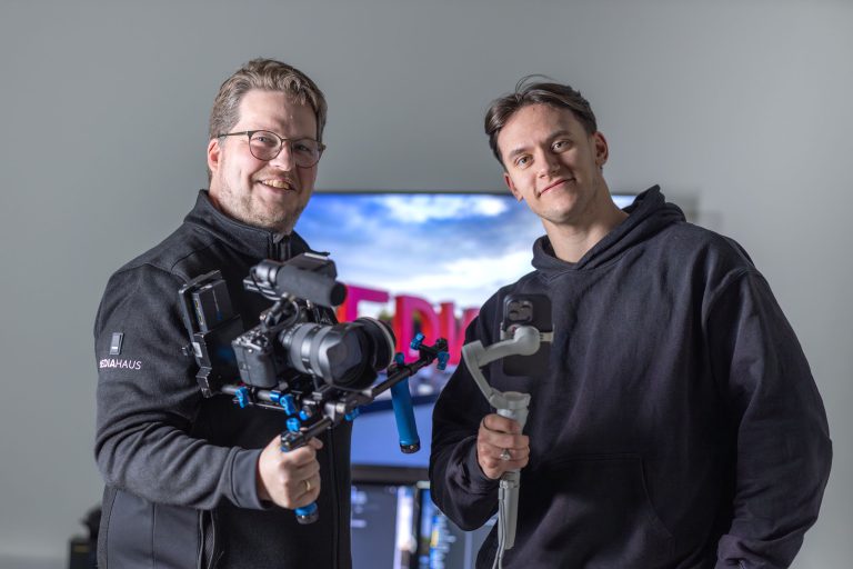 Zwei Mitarbeiter des MEDIAHAUSES mit einer Videokamera und einem Handy in der Hand.