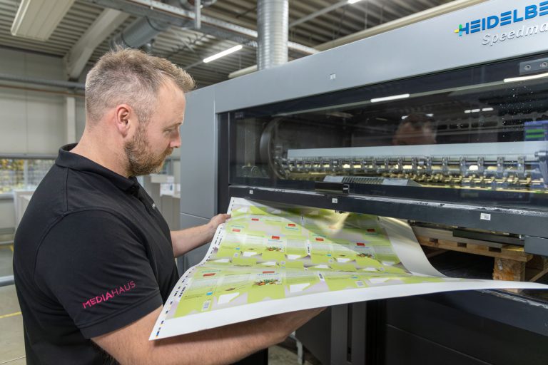 Mitarbeiter des MEDIAHAUSES der einen Testdruck für Verpackungen frisch aus der Druckmaschine holt.