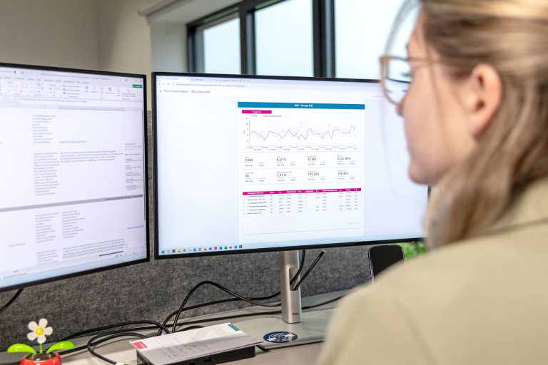 Mitarbeiterin an Ihrem Arbeitsplatz, die auf Ihren PC-Bildschirmen ein Reporting von Google Ads geöffnet hat.
