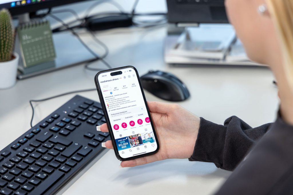 Frau mit Handy in der Hand auf dem die Instagramseite vom MEDIAHAUS zu sehen ist.