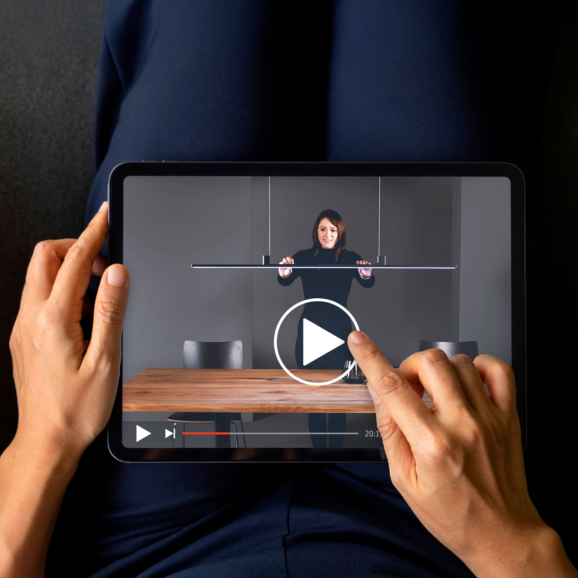 Person mit einem Tablet auf dem Oberschenkeln. Darauf ein Video über eine Hängeleuchte von Bankamp.